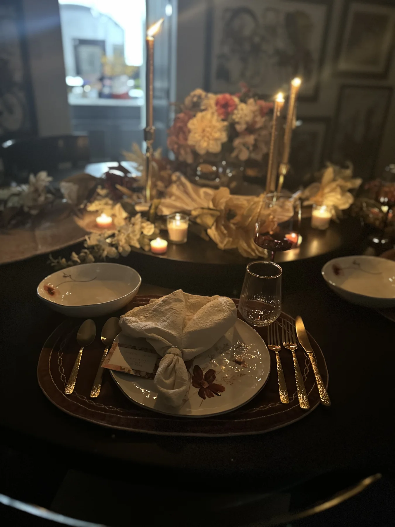 Intimate dinner setting with layered china, gold flatware, and glowing candles